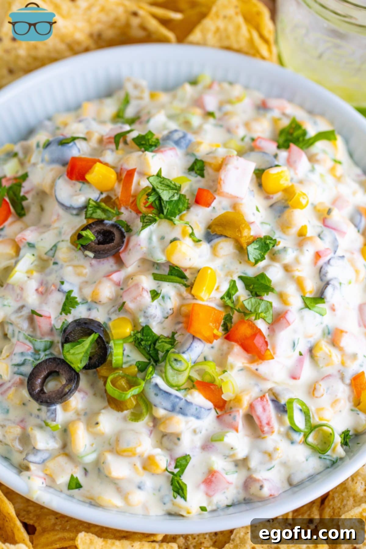 Looking down on a serving bowl of vibrant Poolside Dip, generously garnished with fresh herbs and a lime wedge, surrounded by a variety of crispy chips ready for dipping.