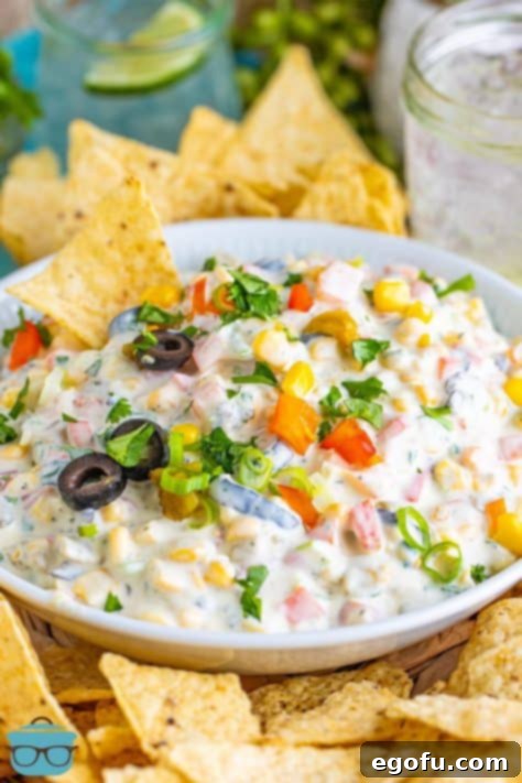 A beautifully garnished serving bowl of Poolside Dip, surrounded by a variety of crispy corn chips for dipping.