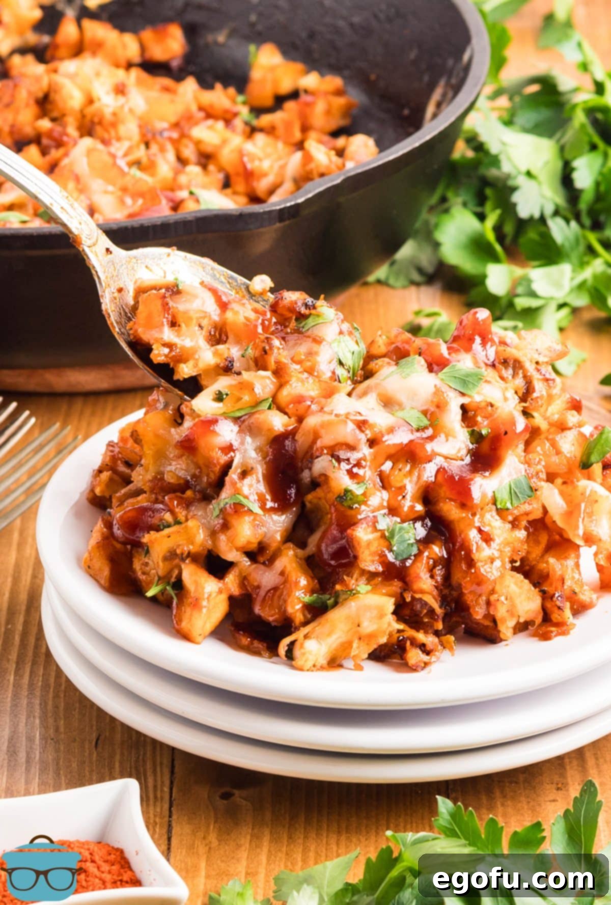 Smoky BBQ Chicken and Crispy Potato Skillet 2 A serving spoon placing some BBQ Chicken Potato Skillet on a stack of white plates.