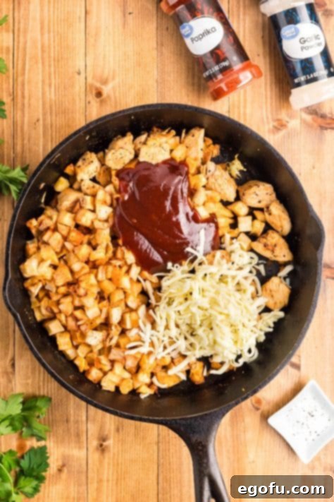 Smoky BBQ Chicken and Crispy Potato Skillet 17 Cheese and bbq sauce on top of chicken and garlic in a skillet.