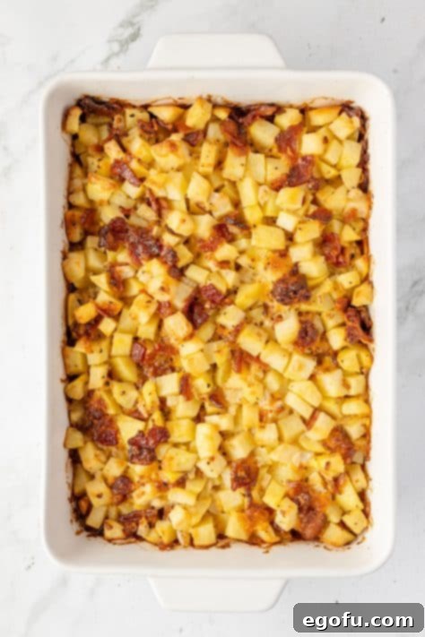 A baking dish with baked potatoes, onion, garlic, bacon, mayonnaise, cheddar cheese, onion powder, garlic powder, salt, and pepper after cooking.