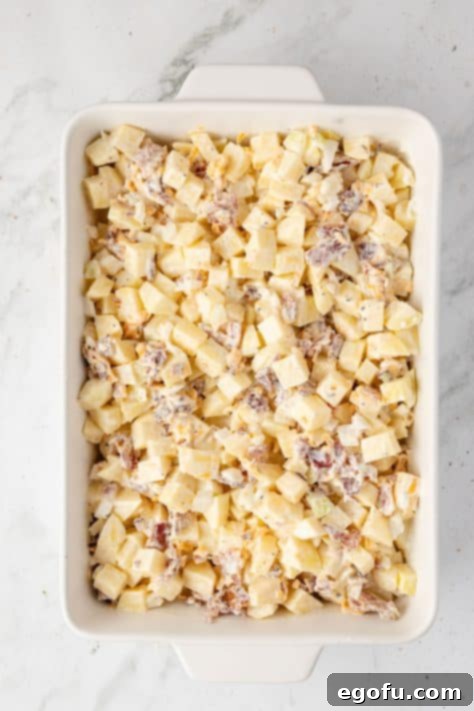 A baking dish with potatoes, onion, garlic, bacon, mayonnaise, cheddar cheese, onion powder, garlic powder, salt, and pepper mixed together.