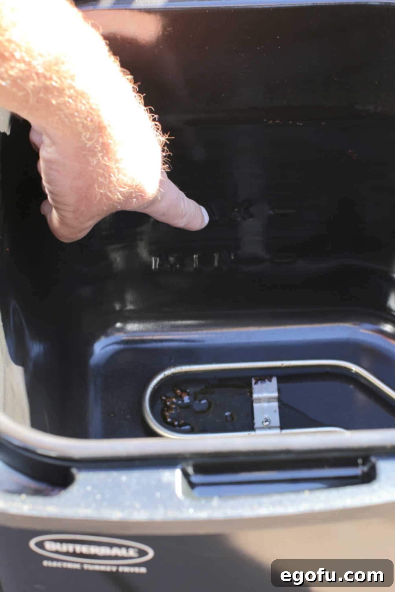 a male finger pointing at a fill line inside a turkey fryer. 