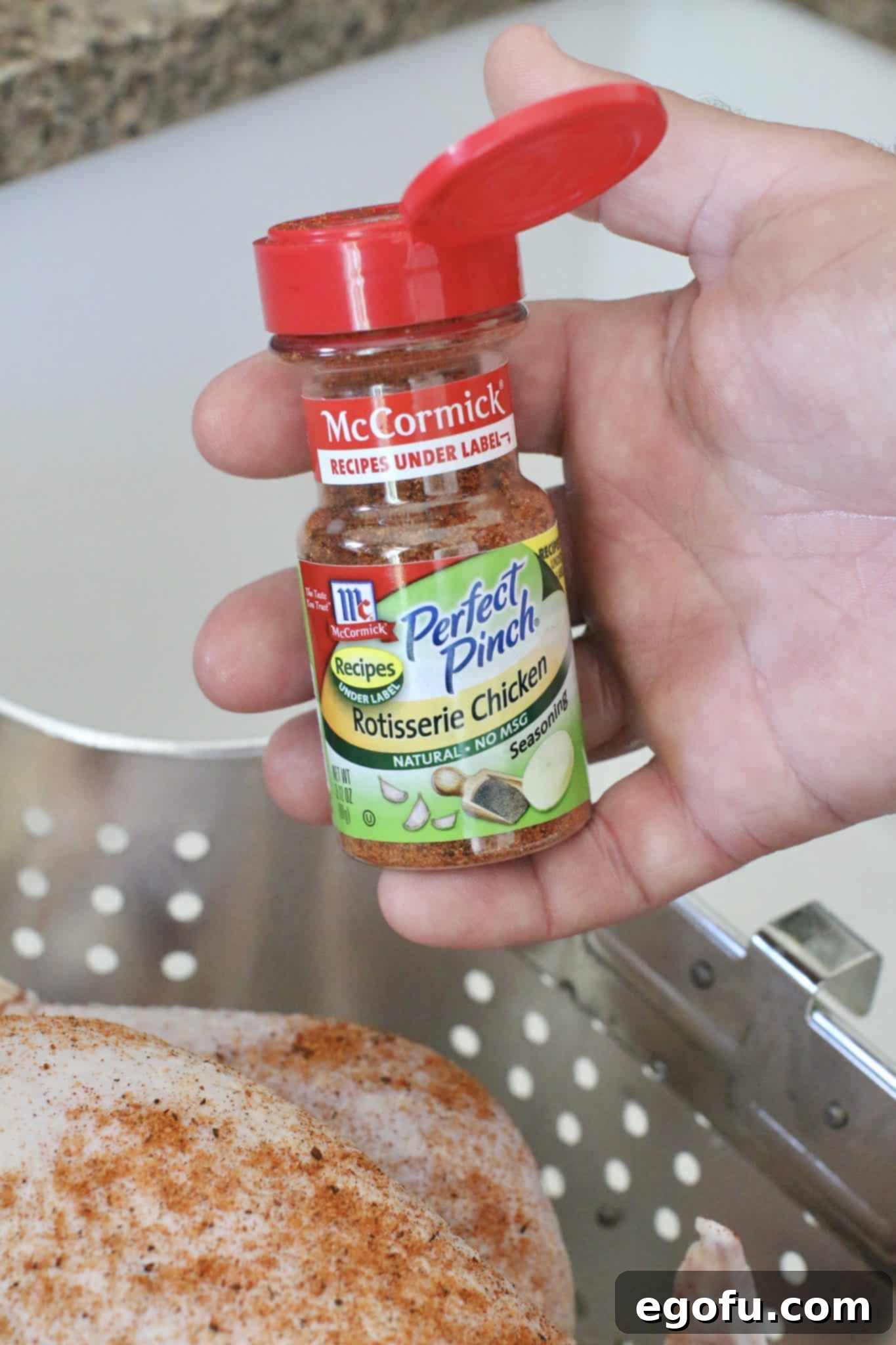 a caucasian male hand holding a bottle of Mccormick Rotisserie Chicken seasoning. 