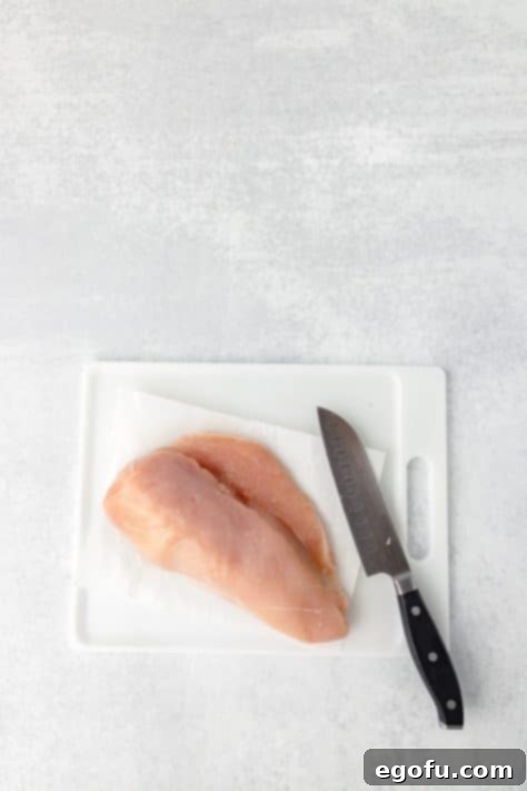 Chicken being cut thin on a cutting board with a knife.
