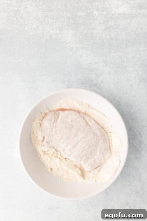 Chicken breast being coated with flour mixture.