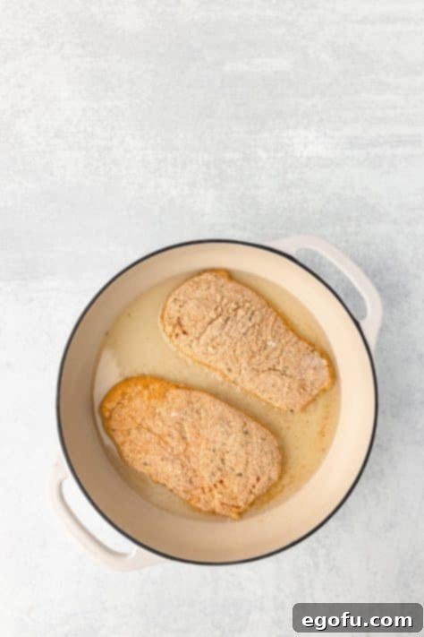 Coated chicken being cooked in oil in a skillet.