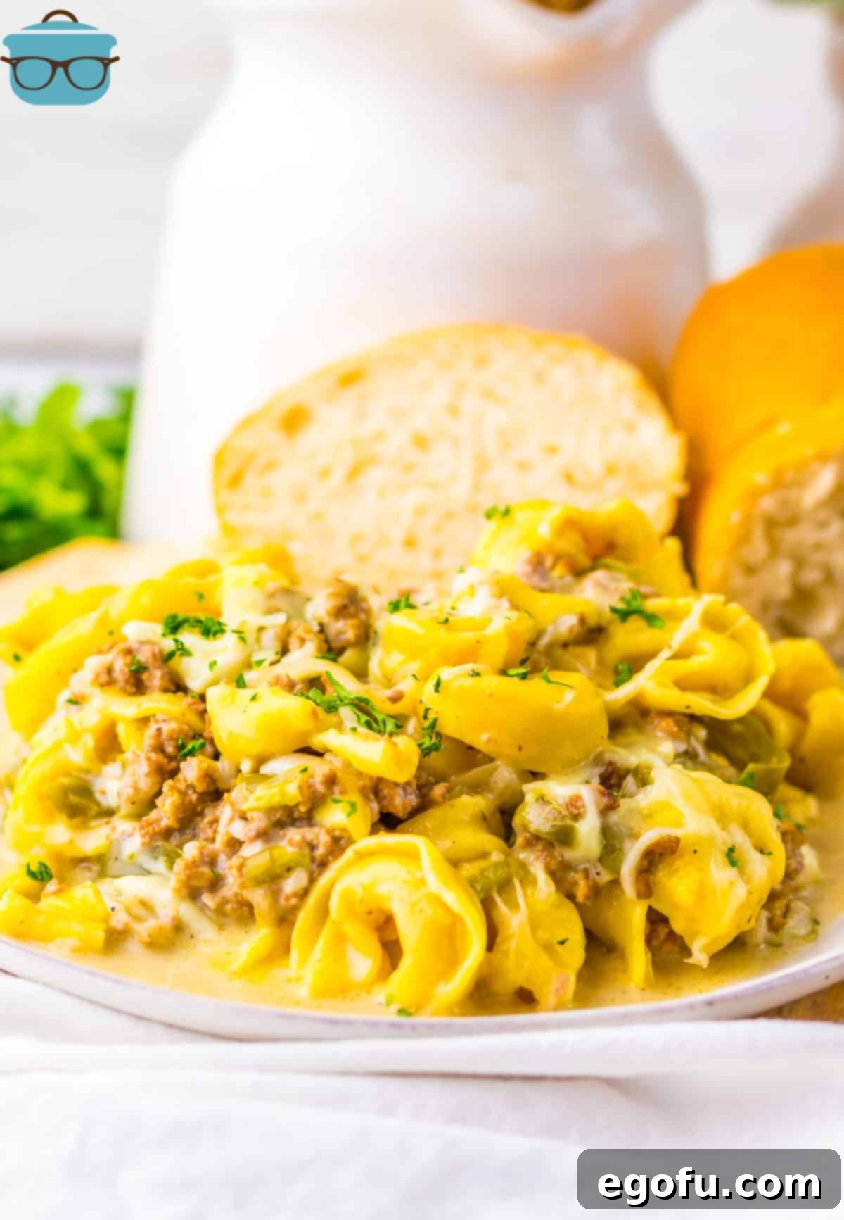 An overflowing plate of Crock Pot Cheesesteak Tortellini and a slice of buttered bread.
