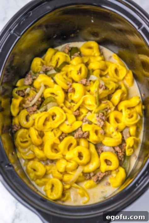 Tortellini with beef, peppers, and onions in a sauce mixture in a Crock Pot.