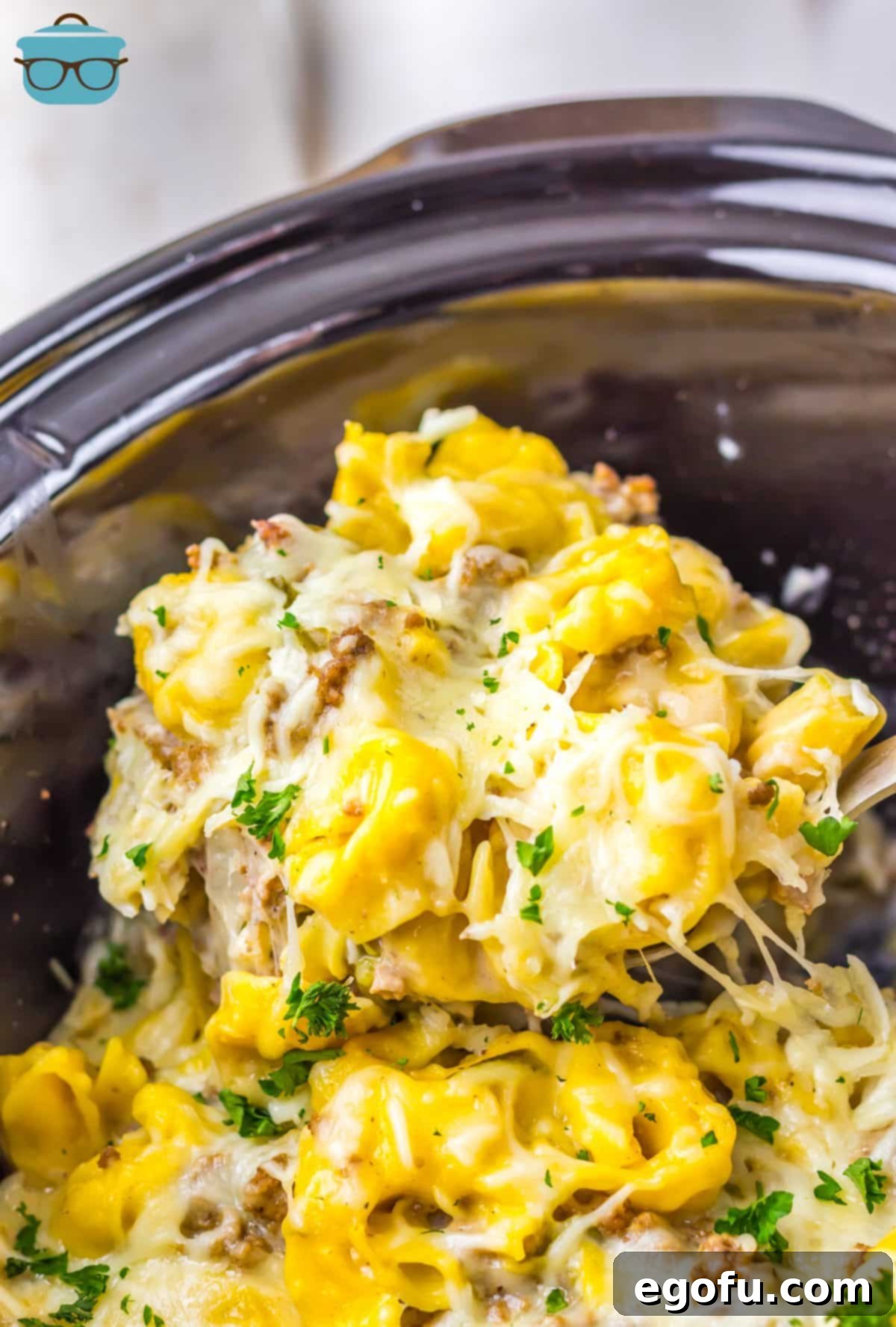 The insert of a Crock Pot with Cheesesteak Tortellini and a scoop being removed.