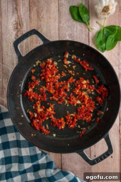 Sundried tomatoes and garlic being cooked in a skillet.