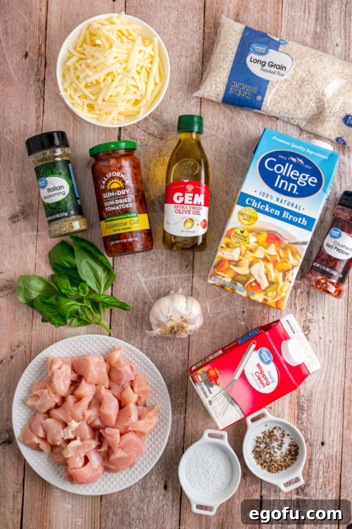 A flat lay of all the ingredients for Marry Me Chicken and Rice, including chicken breast, chicken stock, heavy cream, olive oil, salt, pepper, garlic cloves, sun-dried tomatoes, white rice, Italian seasoning, red pepper flakes, fresh basil, and mozzarella cheese.
