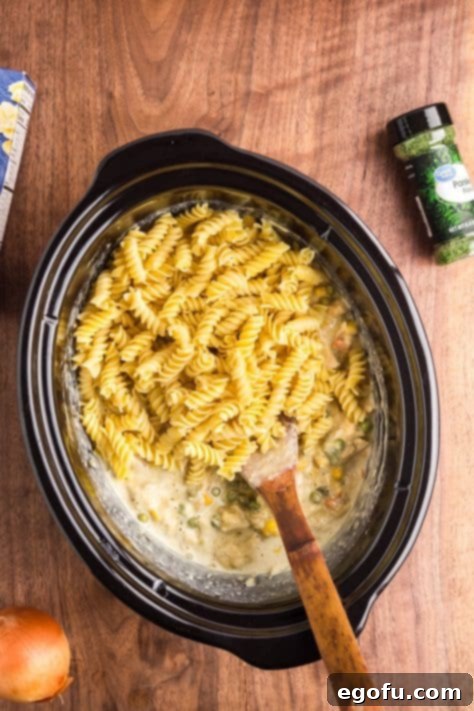 Ultimate Slow Cooker Chicken Pot Pie Pasta 14 Pasta being added to a Slow Cooker chicken mixture.
