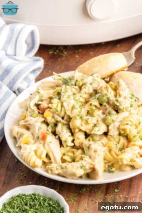 Ultimate Slow Cooker Chicken Pot Pie Pasta 15 A plate with a large serving of Crock Pot Chicken Pot Pie Pasta and a side of bread.