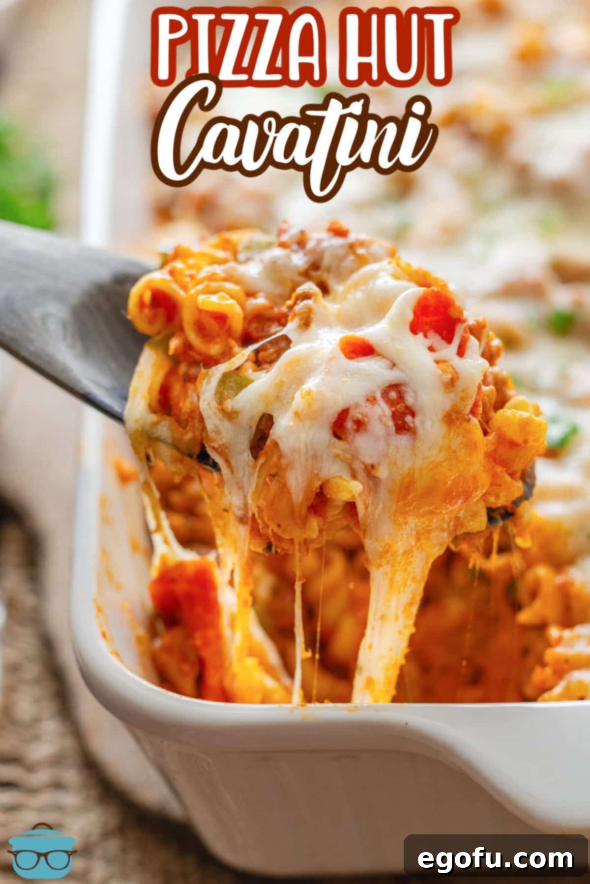 A serving spoon lifts a generous scoop of Pizza Hut Cavatini from the baking dish, showcasing the melted cheese and rich pasta mixture.