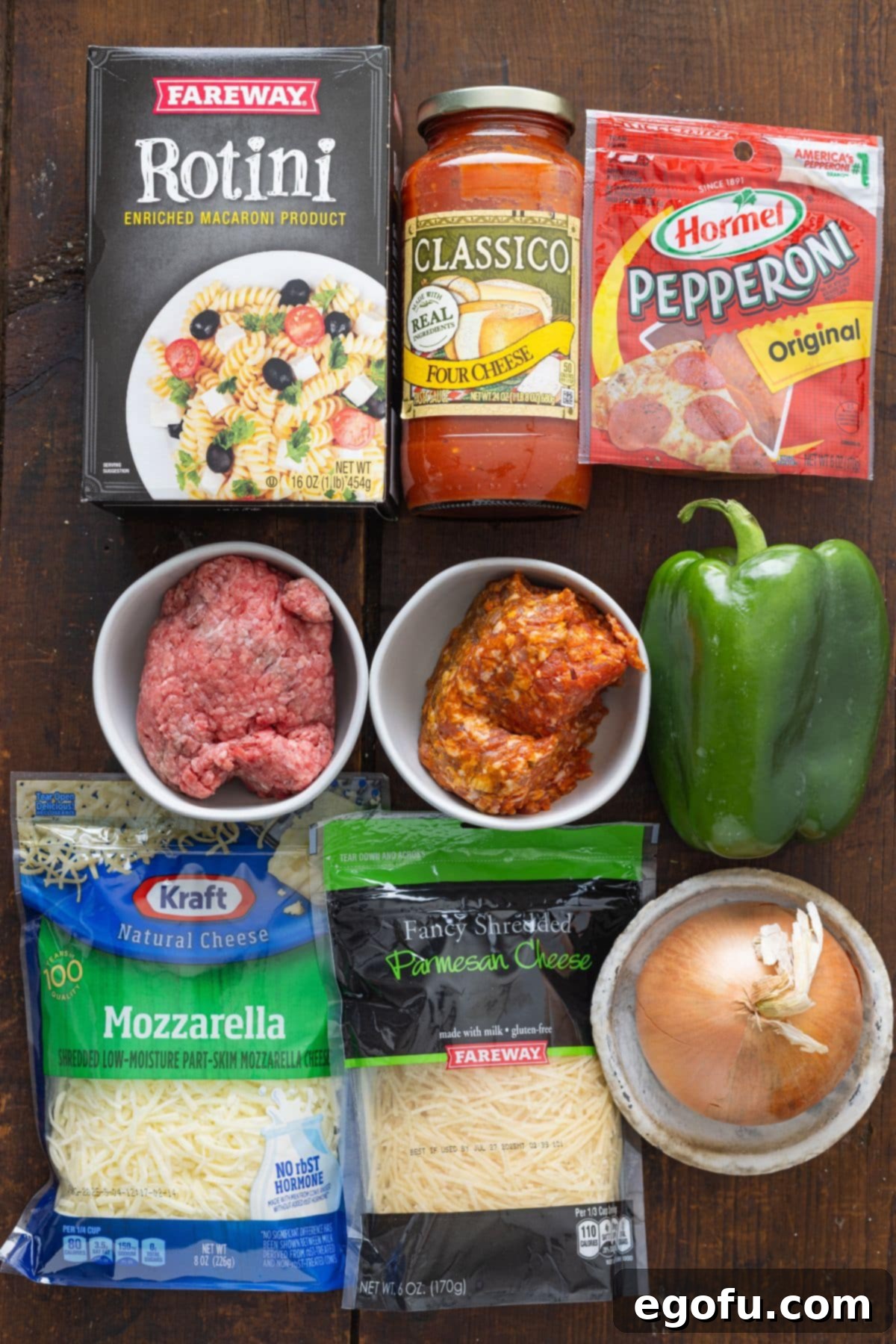 A vibrant flat lay of all the essential ingredients for Pizza Hut Cavatini: rotini pasta, two jars of marinara sauce, a bag of pepperoni, lean ground beef, Italian sausage, diced green bell pepper, diced yellow onion, and two kinds of shredded cheese (mozzarella and parmesan).