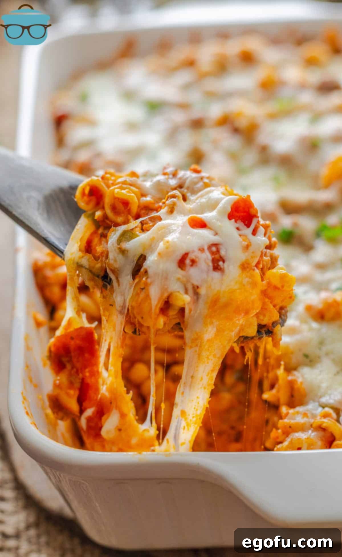 A serving spoon lifts a generous scoop of hot, bubbly Pizza Hut Cavatini from the baking dish, steam rising from the melted cheese and rich pasta.