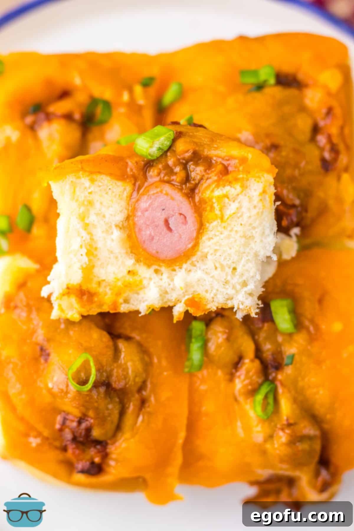 A cut Chili Cheese Dog Slider on top of a few other topped sliders, showcasing the melted cheese and chili.