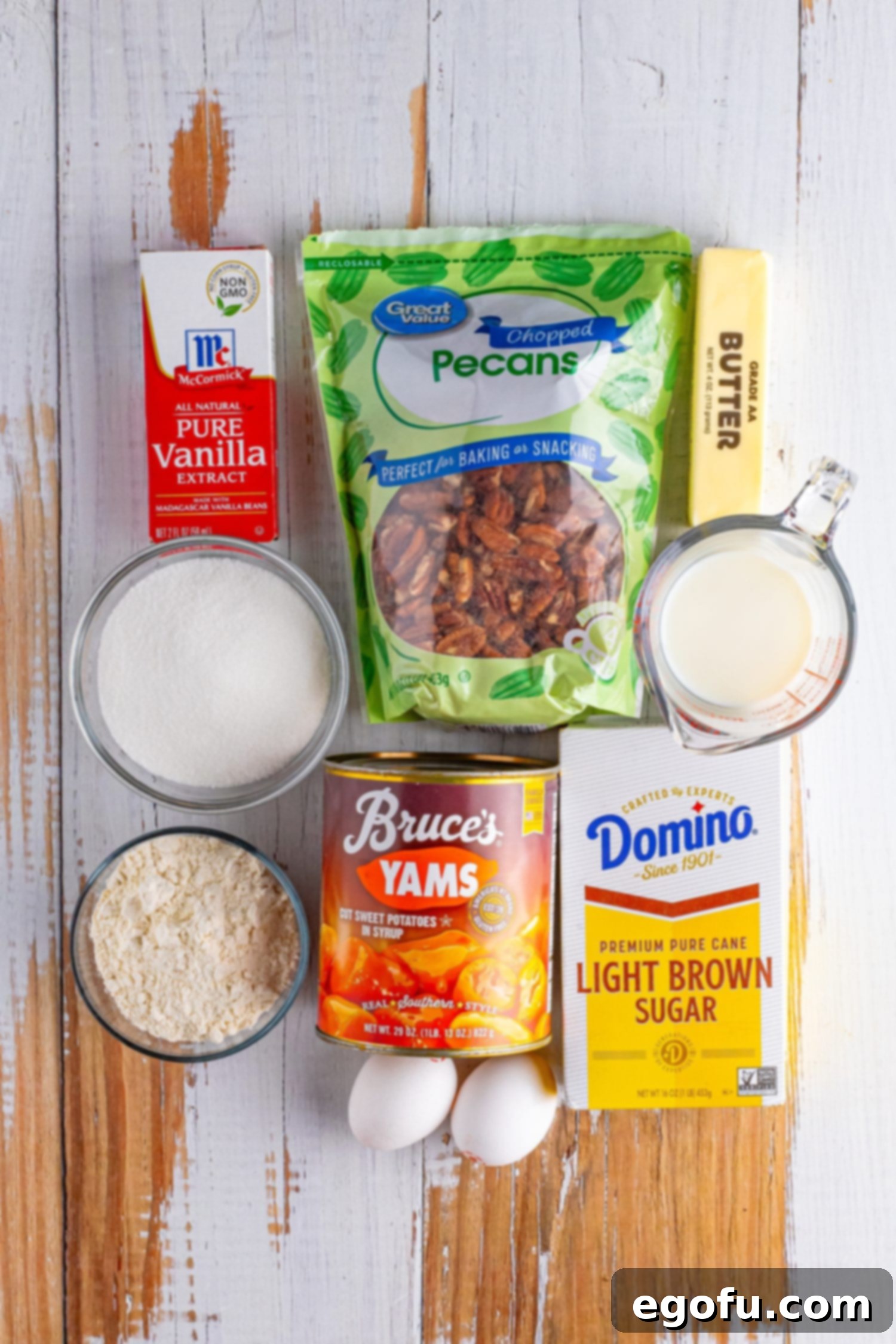 Individual ingredients laid out: Pecans, brown sugar, white sugar, eggs, vanilla, butter, flour, canned sweet potatoes, and milk, ready for preparation.