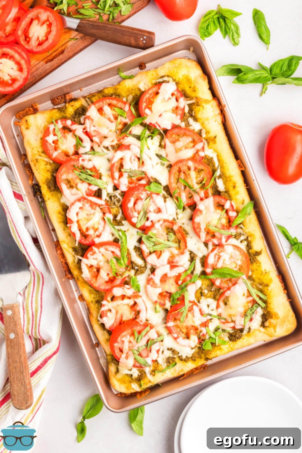 An overhead shot of a freshly baked Slab Tomato Pie on a baking sheet, showcasing the vibrant red tomatoes, green pesto, and melted mozzarella cheese, ready to be served.