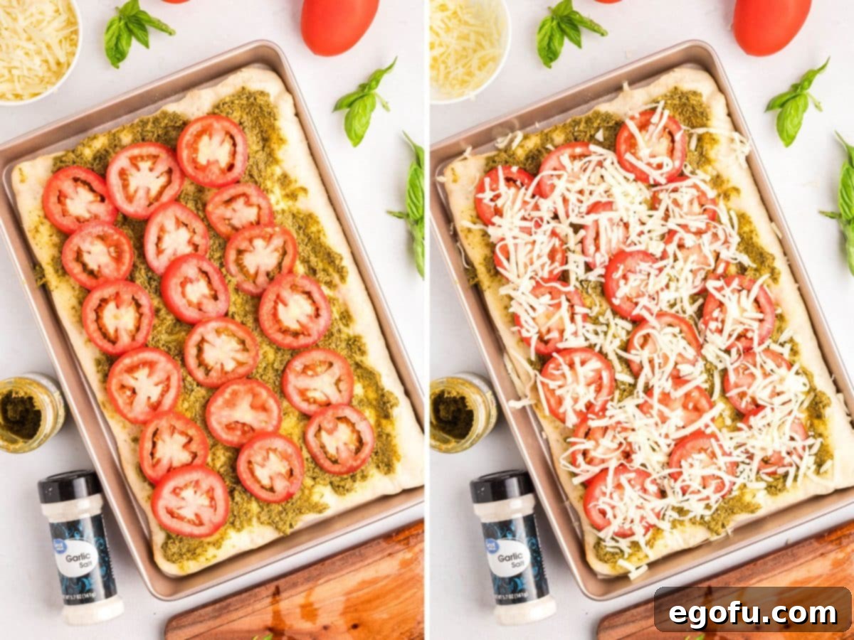 A prepared pizza crust topped with a layer of green pesto, followed by overlapping slices of red tomatoes, and finally a generous sprinkle of white shredded mozzarella cheese, ready for baking.