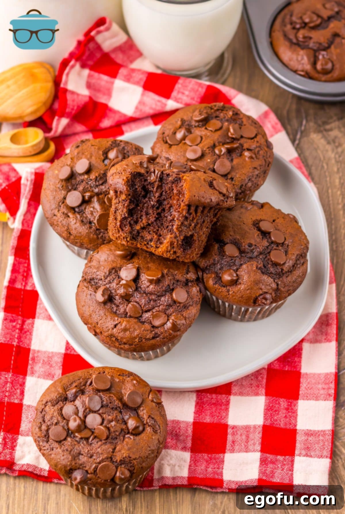 A plate with a few homemade Costco Double Chocolate Muffins, one with a bite taken out, showing its moist interior and abundant chocolate chips.