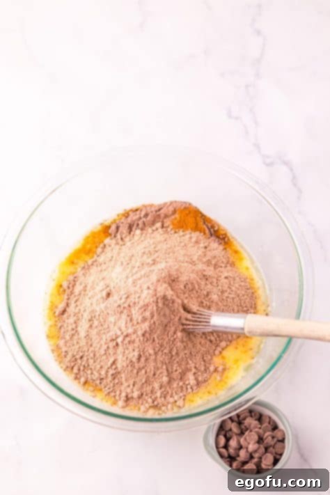 A bowl with chocolate cake mix being added to wet ingredients for muffin batter.
