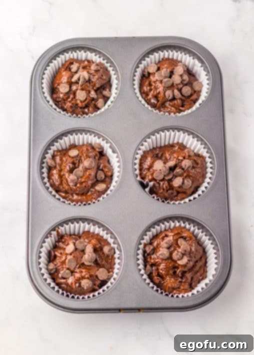 Muffin batter with chocolate chips in a lined muffin pan, ready for baking.