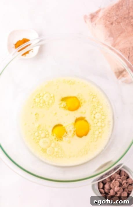 A bowl with eggs, oil, milk, water, and vanilla extract being mixed.
