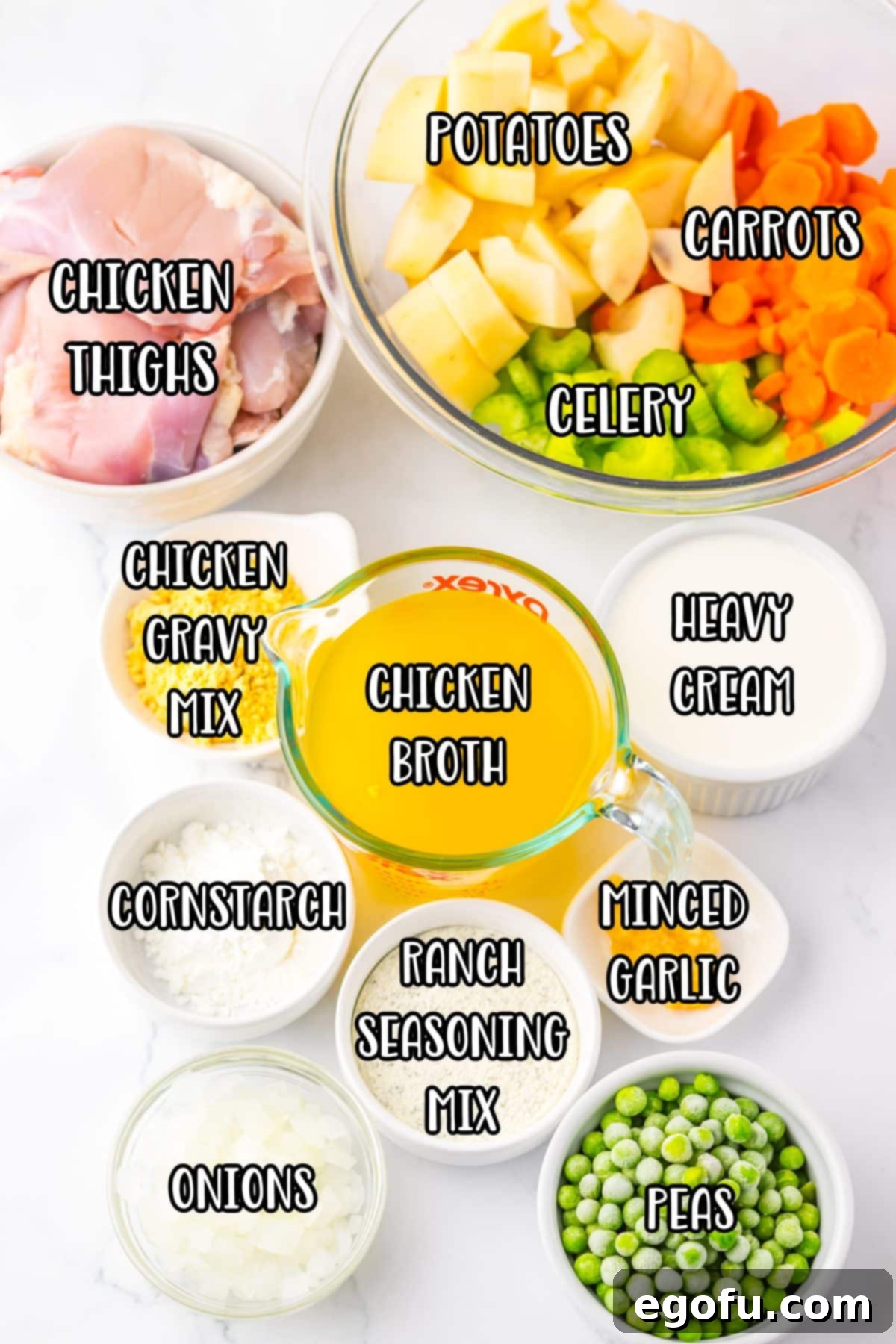 A vibrant flat lay of all the fresh ingredients needed for Crock Pot Chicken Stew: chicken thighs, chicken broth, chicken gravy mix, heavy cream, celery, potatoes, carrots, minced garlic, frozen peas, and onions.