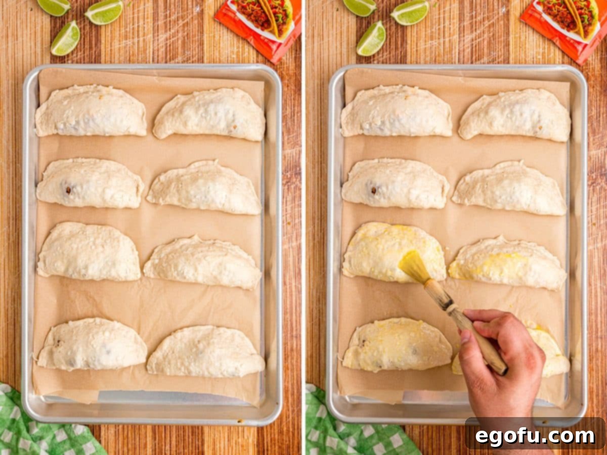 All the unbaked Taco Pockets on a sheet pan being brushed with an egg wash.