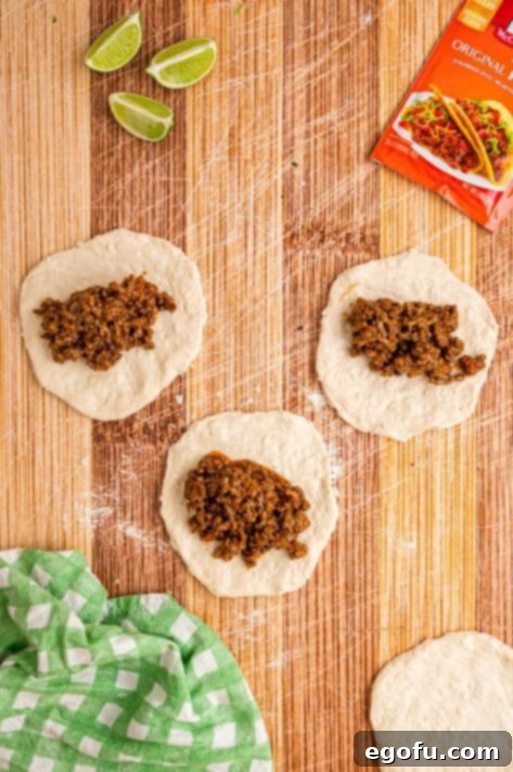 Taco beef mixture placed on rolled out biscuit dough pieces.