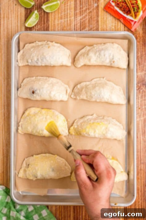 Sealed Taco Pockets on a baking sheet, being brushed with egg wash.