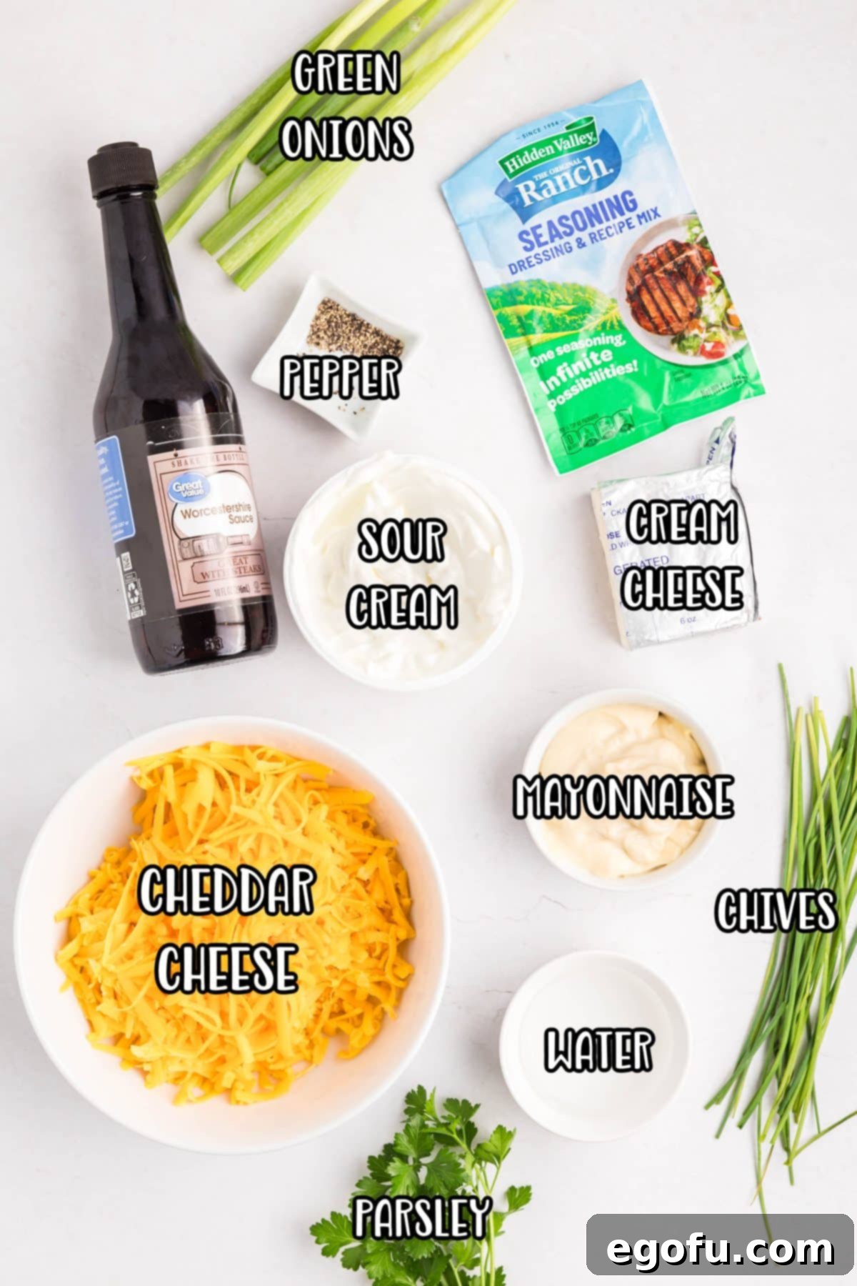 Individual ingredients for Pontoon Dip laid out: Worcestershire sauce, green onions, ranch seasoning, black pepper, sour cream, cream cheese, chives, parsley, water, and shredded sharp cheddar cheese.