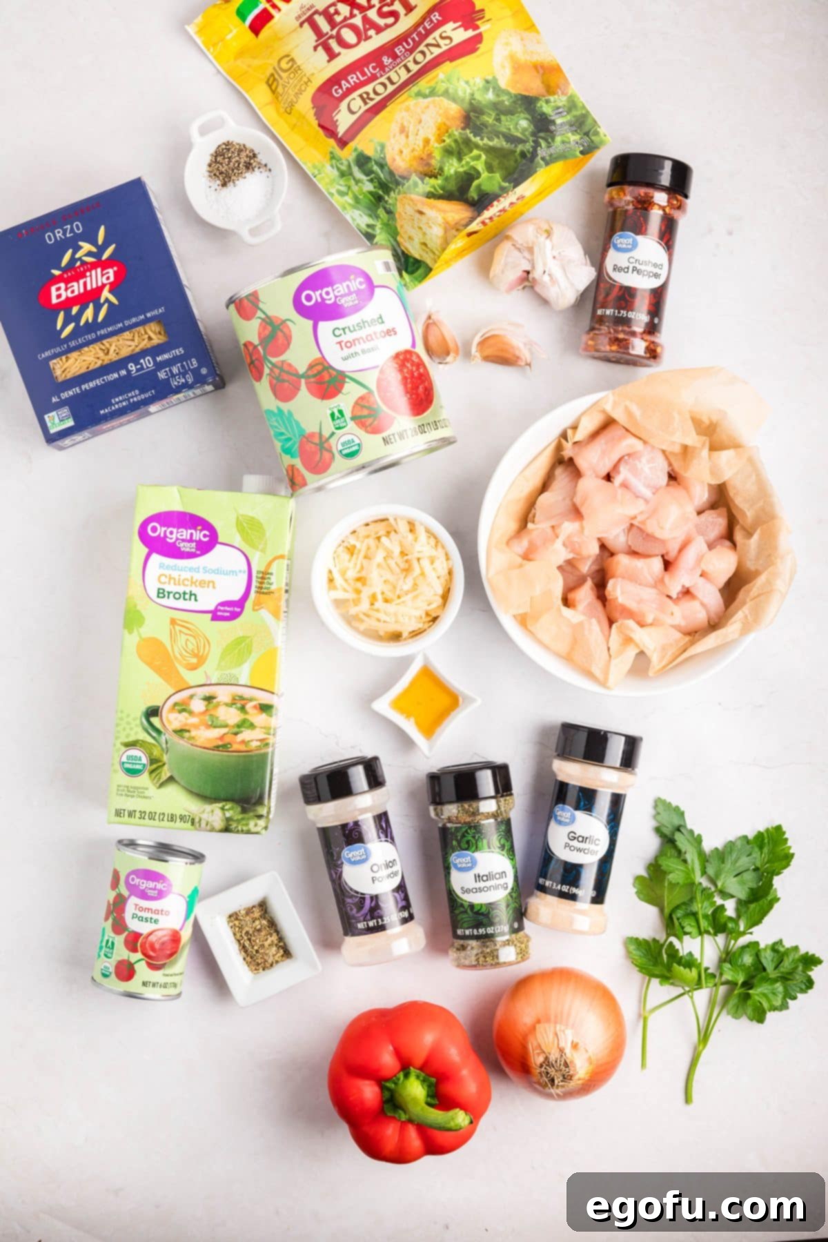 A flat lay photograph showcasing all the fresh and pantry ingredients laid out for making Crock Pot Chicken Parmesan Soup, including chicken, vegetables, spices, broth, and garnishes.