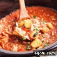 Close up view of a wooden serving spoon getting a scoop of Crock Pot Chicken Parm Soup, showing the rich texture and ingredients.