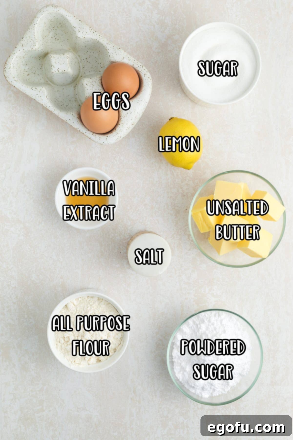 A flat lay of all the essential ingredients for homemade lemon brownies: powdered sugar, all purpose flour, salt, unsalted butter, fresh lemons, vanilla extract, eggs, and granulated sugar.