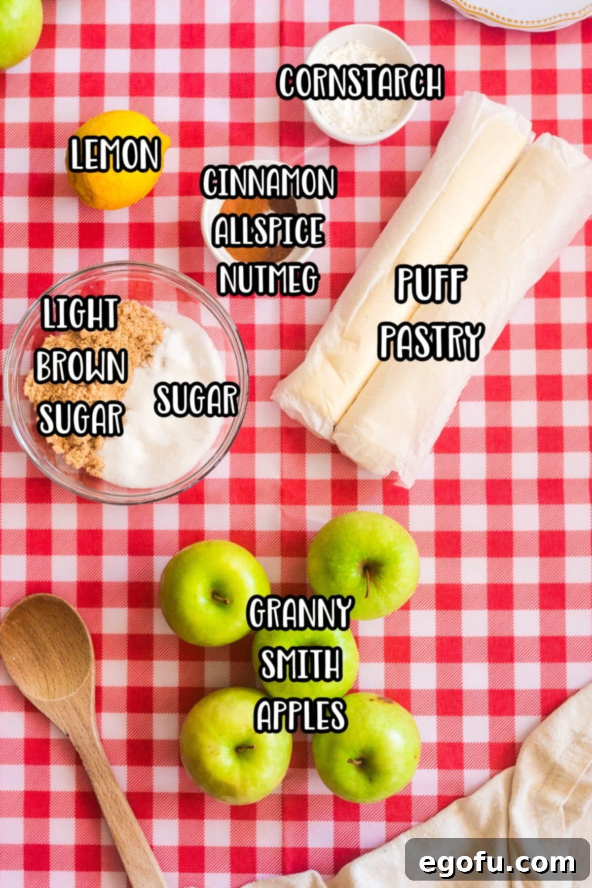 A flat lay of all the essential ingredients: puff pastry, Granny Smith apples, sugars, lemon, cinnamon, allspice, and nutmeg, neatly arranged for making apple pies.