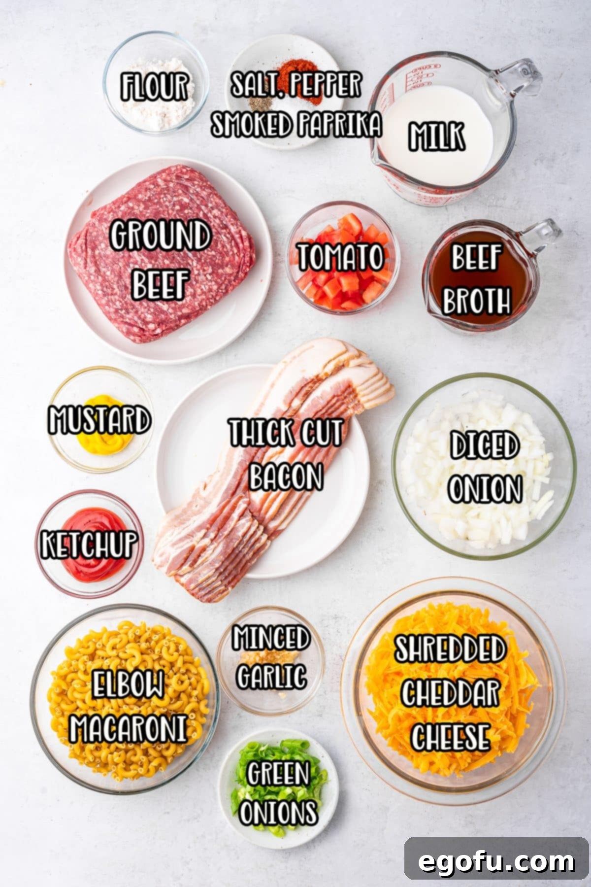 Cheesy Bacon Burger Bake 4 An organized display of all raw and prepped ingredients for Bacon Cheeseburger Casserole, including ground beef, thick-cut bacon, elbow macaroni, shredded cheddar cheese, yellow onion, garlic, ketchup, mustard, beef broth, milk, and spices.