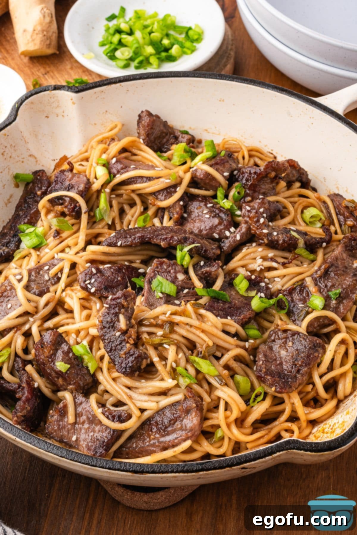 A large pot filled with steaming Mongolian Beef Noodles, garnished with fresh green onions and sesame seeds, ready to be served.
