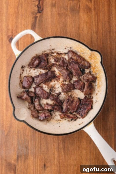 Cooked cornstarch coated beef in a skillet.