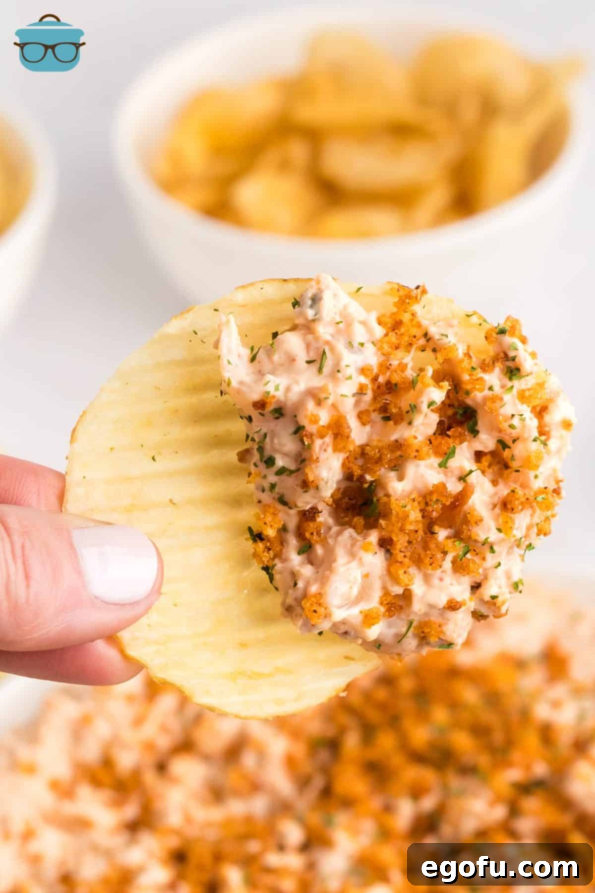 A potato chip with some Homemade Bloomin' Onion Dip on it, showcasing its creamy texture and breadcrumb topping.