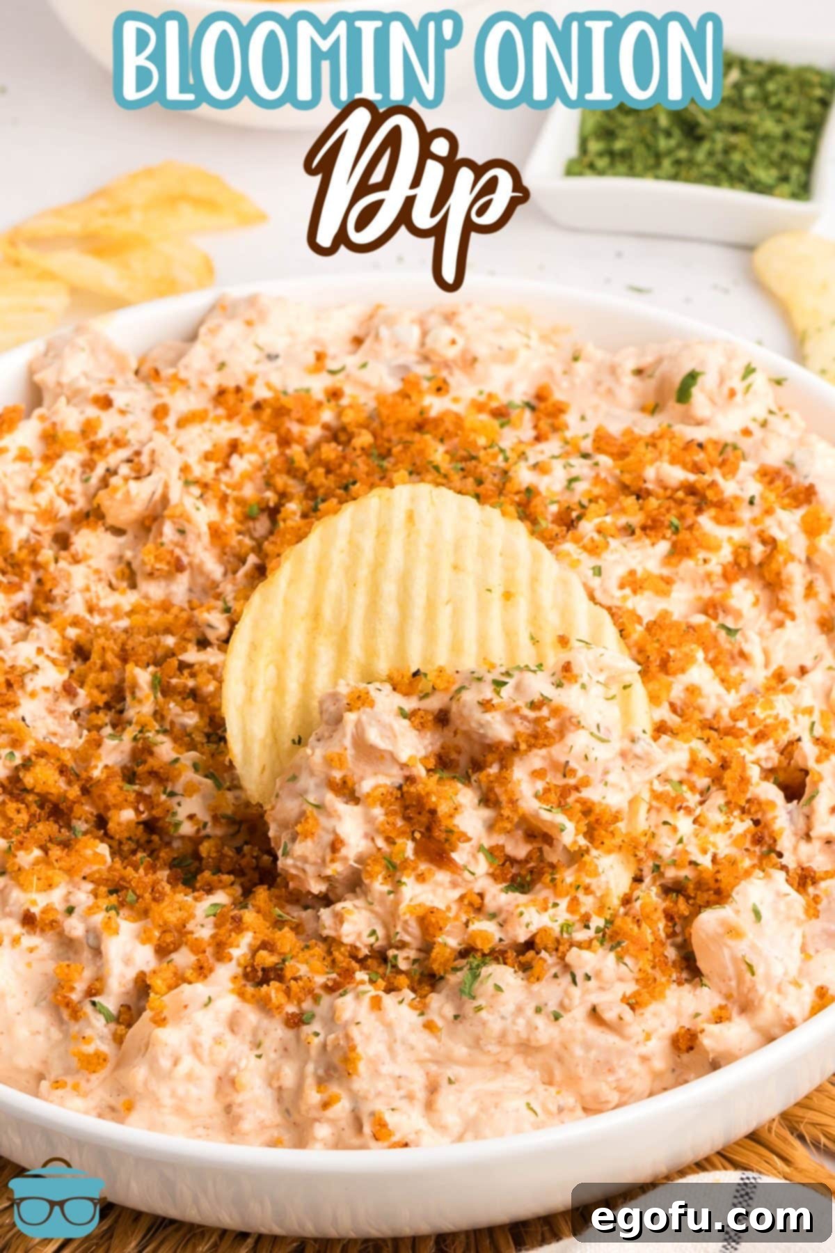 A chip dipped into a large serving bowl full of Bloomin' Onion Dip, garnished with parsley and breadcrumbs.