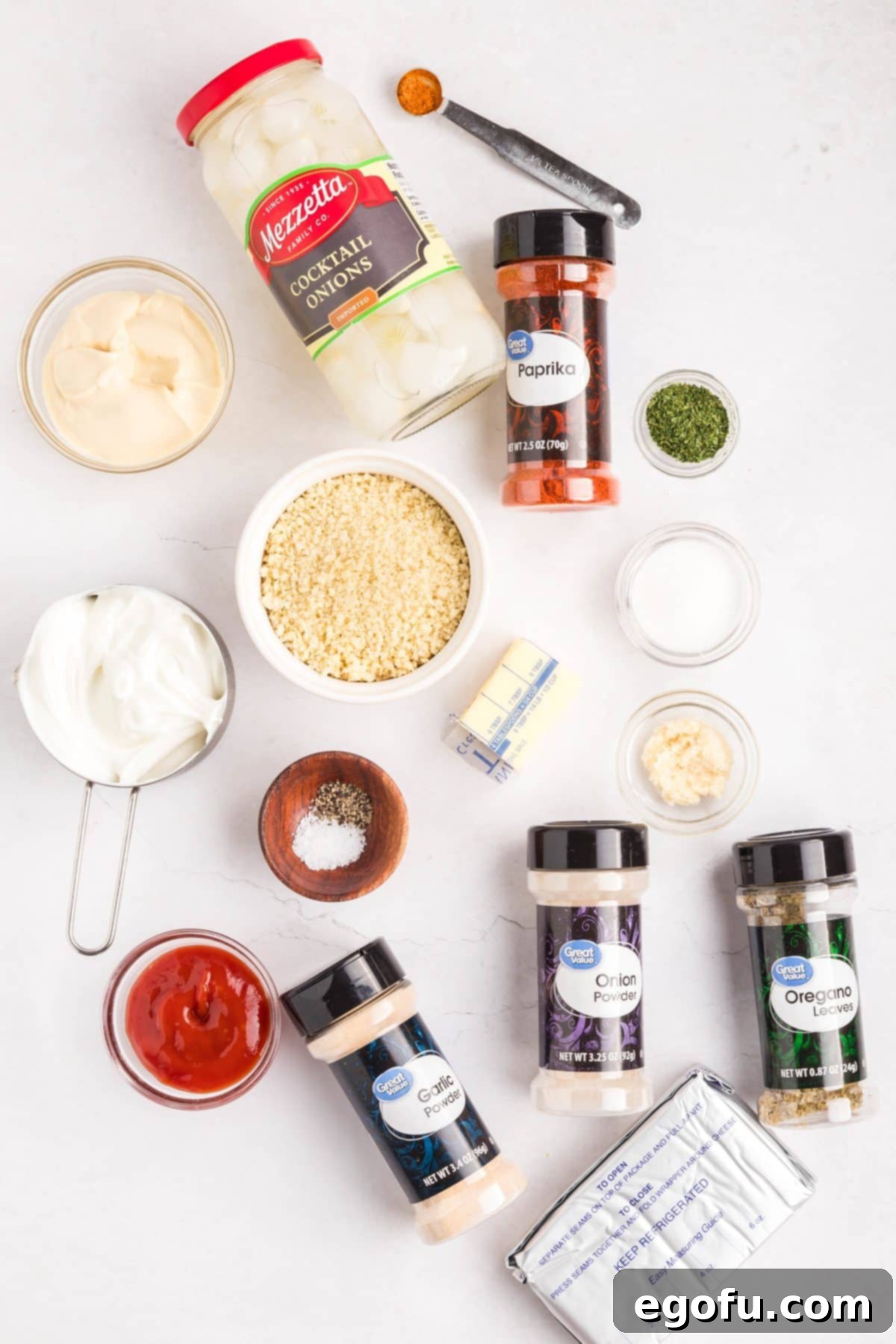 All ingredients laid out on a table: butter, panko breadcrumbs, various spices (onion powder, garlic powder, paprika, pepper, salt, oregano, cayenne), cocktail onions, cream cheese, sour cream, mayonnaise, ketchup, sugar, and dried parsley.