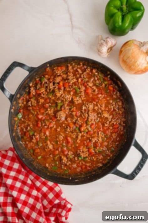 Ground beef, veggies, tomato sauce, diced tomatoes, and spices in a skillet.