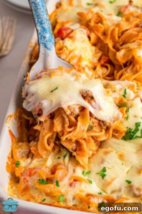 Closely looking down on a baking dish with a scoop of Beef Noodle Casserole being removed.