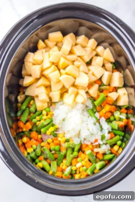 A Crock pot with chicken, onion, potatoes and mixed vegetables.