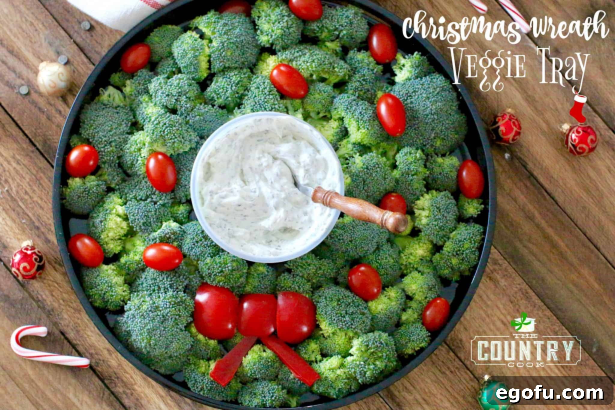 a wreath made our of broccoli, red peppers and grape tomatoes with a vegetable dip in the middle.