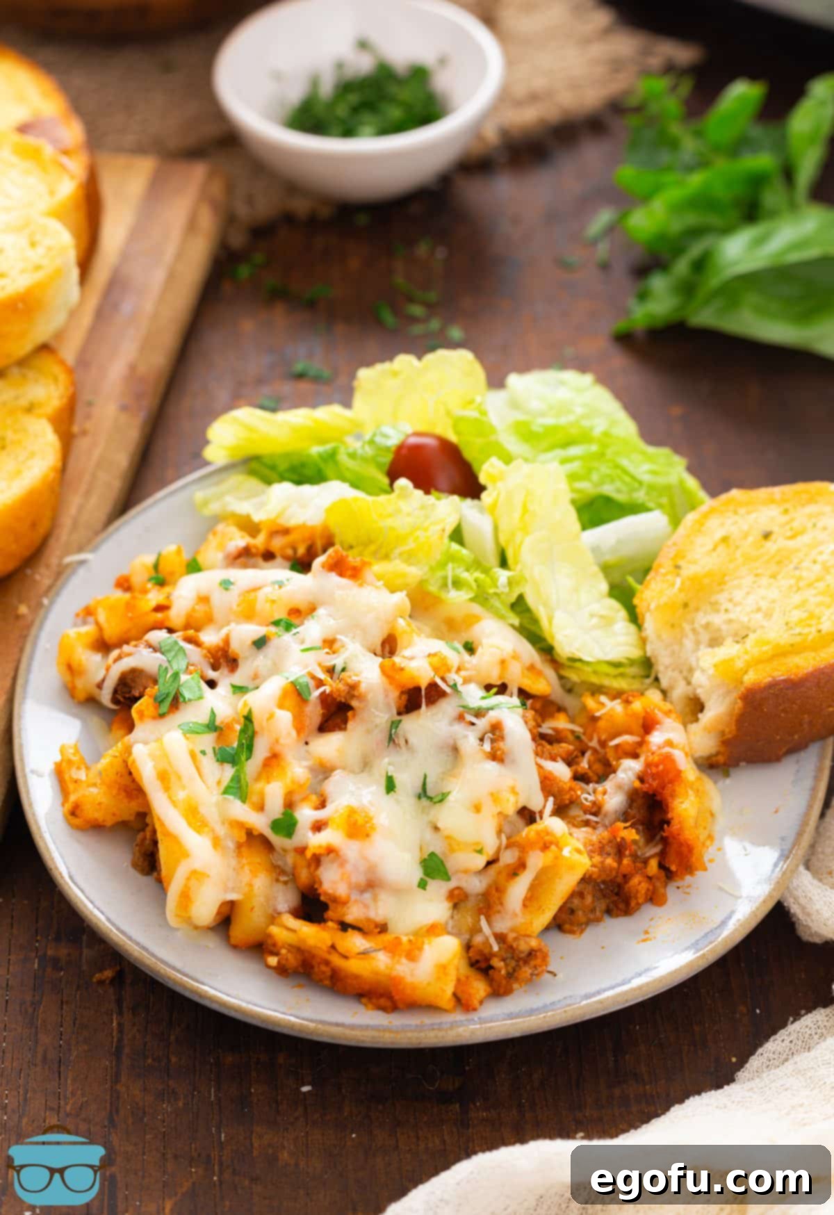 A perfectly plated serving of Crock Pot Baked Ziti, garnished with fresh parsley, alongside a crisp green salad and slices of garlic bread, ready to be enjoyed.