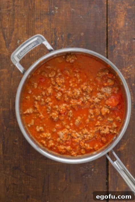 Rich meat sauce simmering in a skillet, combining browned ground beef, marinara, and water, ready for layering.